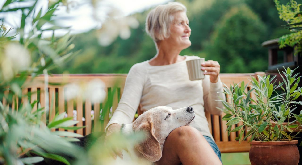 Frau mit Hund auf Bank genießt die frische Luft als Teil ihrer Morgenroutine